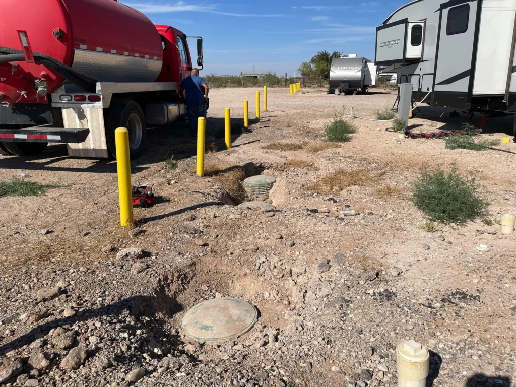 Red vacuum truck and pumping hoses positioned beside wastewater treatment access tanks during a service operation